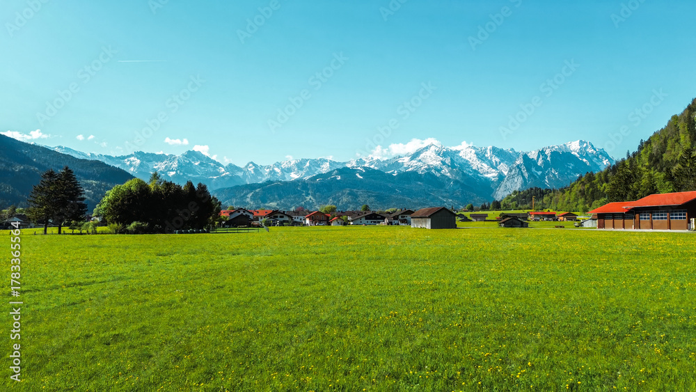 Obraz premium Lush field with rustic cabins and Alps