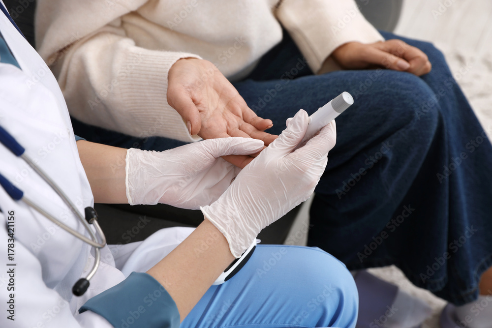 Fototapeta premium Diabetes. Doctor in medical gloves checking patient's blood sugar level with lancet pen indoors, closeup