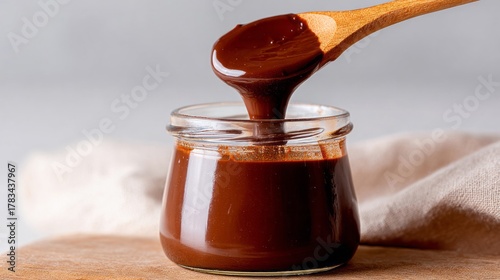 Rich chocolate sauce cascading from wooden spoon into jar, ideal for Chocoholics Day celebrations, evokes velvety indulgence