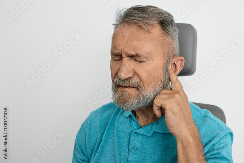 Elderly man experiences discomfort touching his ear, showing signs of hearing loss sitting in ENT clinic indoor