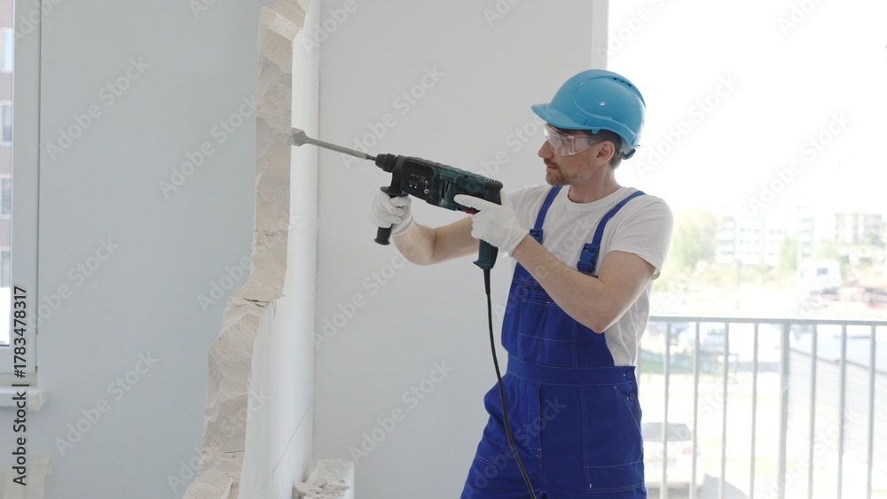 Αυτοκόλλητο Construction worker demolishing concrete wall with rotary hammer, wearing protec