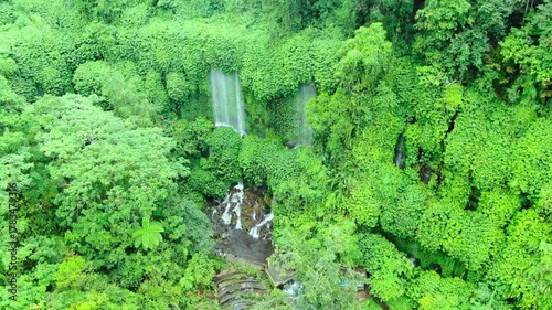 Stable tilt-up shot of a high waterfall in a tropical forest stream over rocks as water falls freely among trees and lush green plants at Benang Stokel tourist spot in Lombok