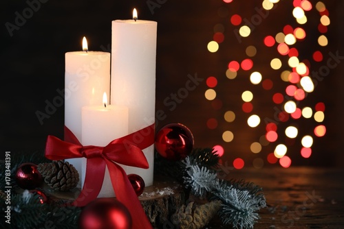 Fototapeta Naklejka Na Ścianę i Meble -  Burning candles, fir tree branches and baubles on wooden table against black background with blurred lights, closeup with space for text. Christmas greeting card