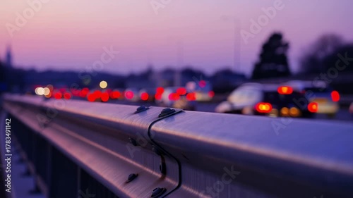 Evening traffic captured with a guardrail in the foreground. Blurred lights of vehicles create a sense of motion against the soft hues of the sky.  Stock Video