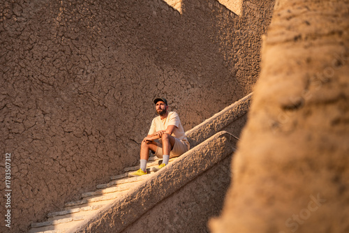 Young man relaxing on ancient mudbrick stairs in sunset oman