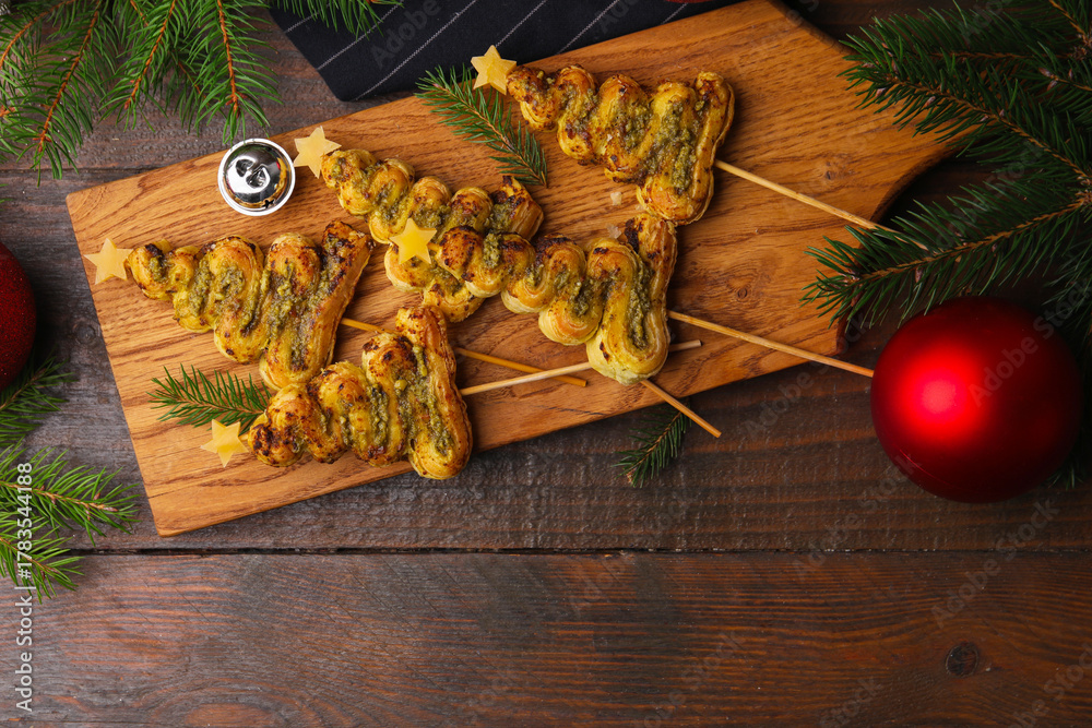 Obraz premium Christmas trees made with puff pastry, pesto sauce, cheese and festive decor on wooden table, flat lay. Space for text