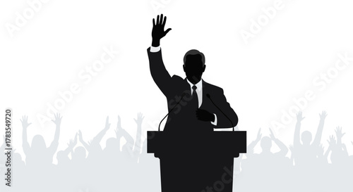 A speaker in a suit at a podium, raising their hand, with an audience cheering behind