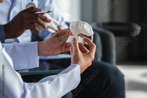 Close-up of dentists discussing a dental model for oral healthcare education in a modern clinic, showing professional teamwork, dental consultation, and medical training with precision.