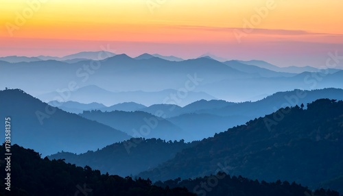 Wallpaper Mural A scenic panorama capturing layers of blue mountains fading into the horizon as the sky transforms with warm sunset hues Torontodigital.ca