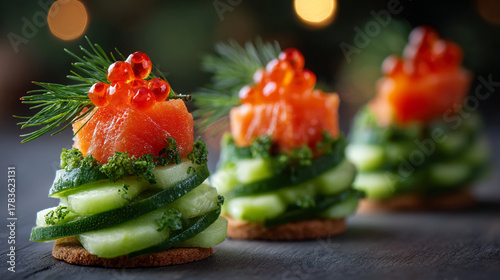 Three salmon and cucumber canapés topped with red caviar and dill on a dark background bokeh lights