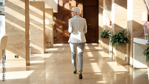 Foto Mature businesswoman walking through modern office building corridor, facing awa