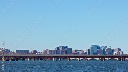 A Washington D.C. Metro train crosses the Potomac River, traveling from Virginia into DC. The skyline of Rosslyn, Virginia, is seen in the background on a clear, sunny autumn day.