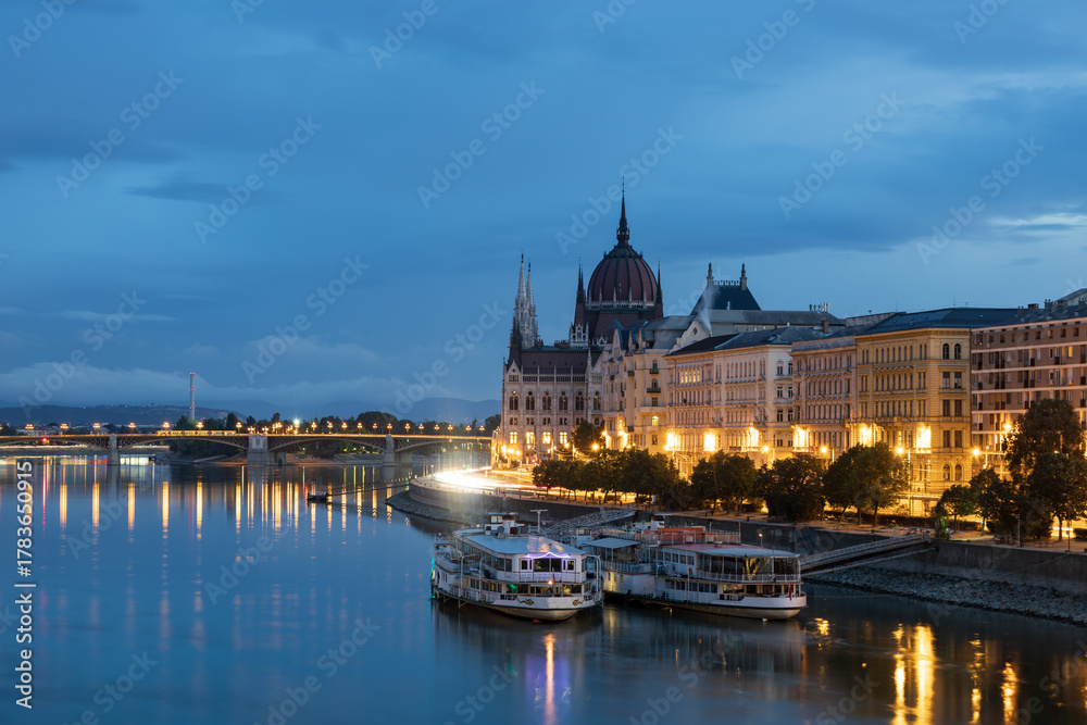 Fototapeta premium Cruise boats moored in the Danube river next to the 1905 Gothic Renaissance style Parliament during a morning blue hour, Budapest, Hungary