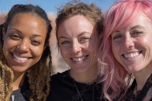 Three women with expressive smiles and diverse hairstyles, sharing a joyful moment outdoors.