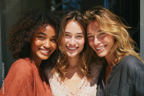 Three diverse women smile warmly, showcasing friendship and happiness outdoors.