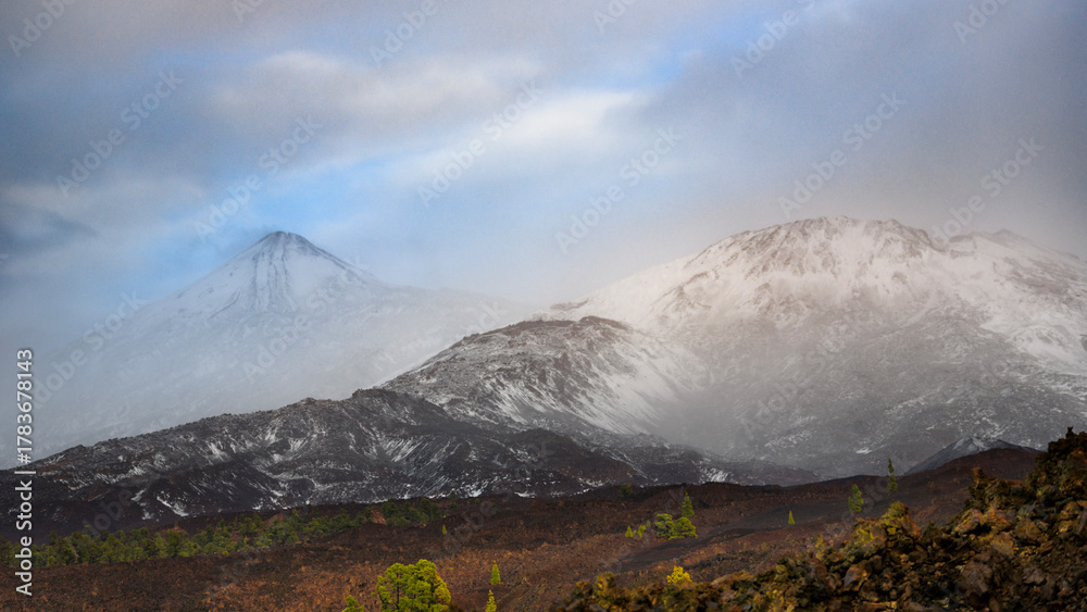 Fototapeta premium Snow-Covered Teide Volcano and Pico Viejo Under Misty Clouds, Tenerife, Canary Islands