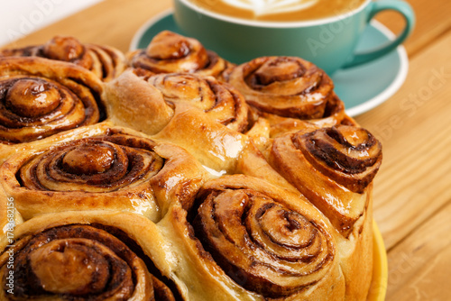 Closeup homemade cinnamon rolls from yeast dough and cup of coffee cappuccino on wooden table. Shallow focus.