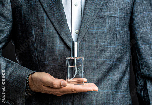 Men perfume in the hand on suit background. Fragrance smell. Men perfumes. Fashion cologne bottle. Man holding up bottle of perfume