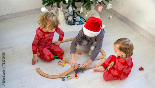Three children playing with a wooden toy train set near the Christmas tree at home