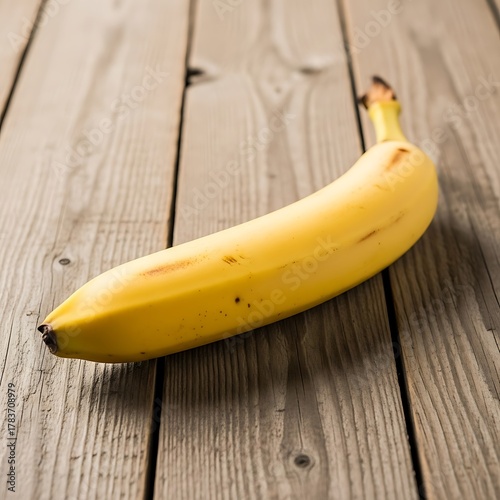 Single ripe banana on rustic wooden surface in natural light.