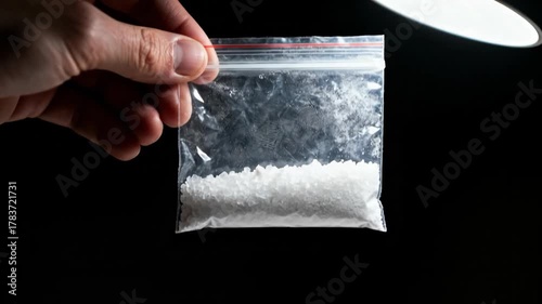 Hand holding a plastic bag of white crystal drugs. Close-up of illegal narcotics with a fingerprint on the bag as evidence. Crime and drug trafficking concept