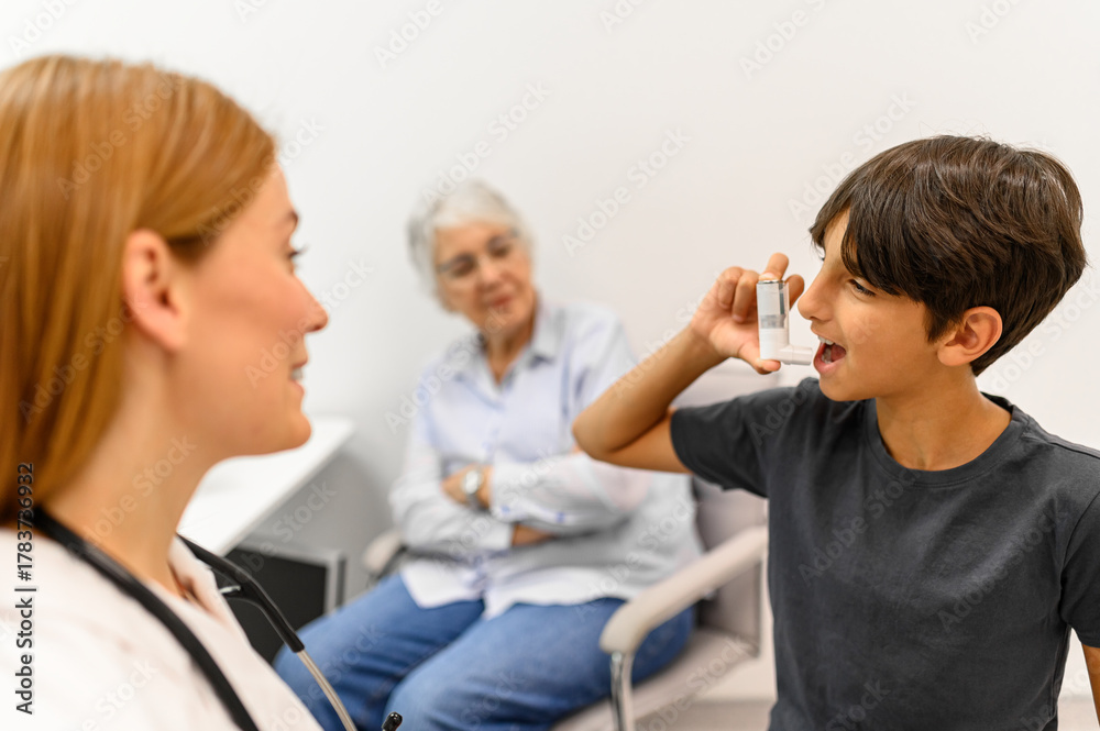 Obraz premium Senior woman and female doctor looking at young boy using inhaler during asthma treatment in clinic