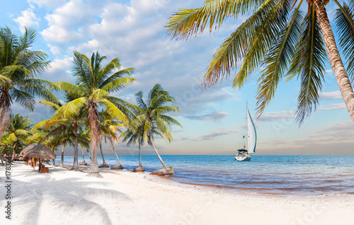 Paradise Sunny beach with palms and turquoise sea with lone yacht - Summer vacation and tropical beach concept - Cancun, Mexico