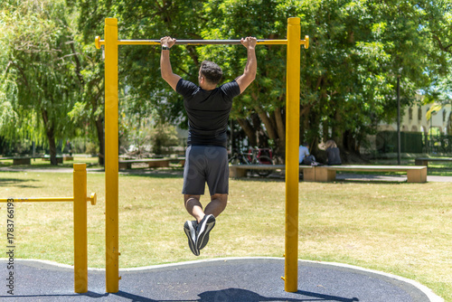 Photography Rear view of young man doing pull ups on a crossbar at a park