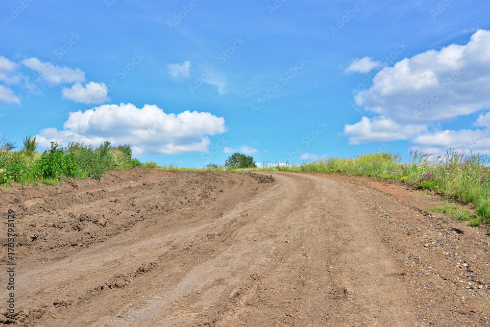 Fototapeta premium empty and Winding Dirt Road with tire track Through Green Hills Under a Blue Sky