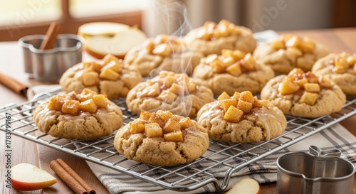 Warm apple cinnamon cookies with diced caramelized apple topping cooling on a wire rack, surrounded by fresh apple slices and cinnamon sticks.