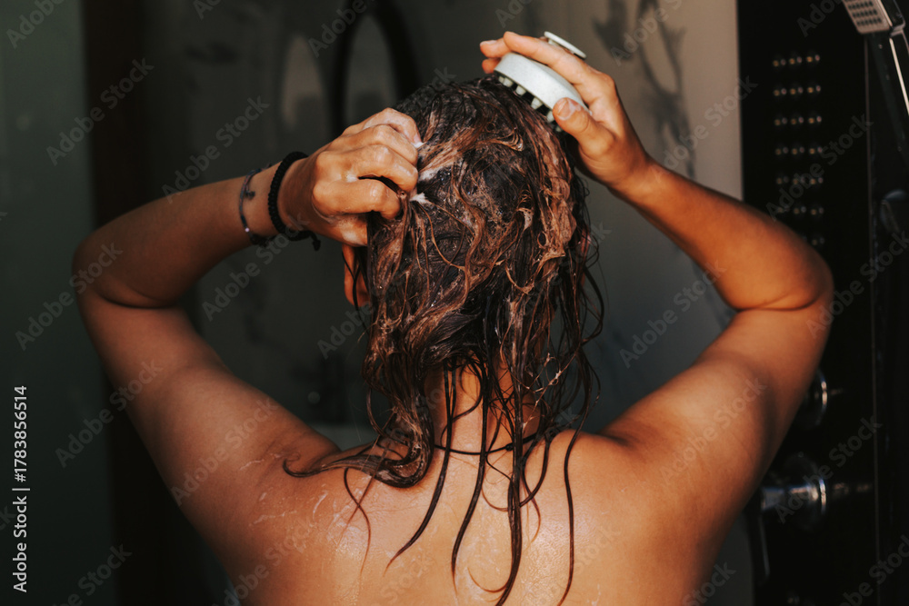 Naklejka premium Woman washes her hair with shampoo and massages head with a hair growth brush. Concept of hair care and the use of conditioner and mask to moisturize