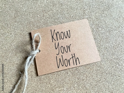 The phrase 'KNOW YOUR WORTH' written on a brown paper tag with string. Represents self-esteem, self-respect, personal value, and self-advocacy in personal or professional settings.