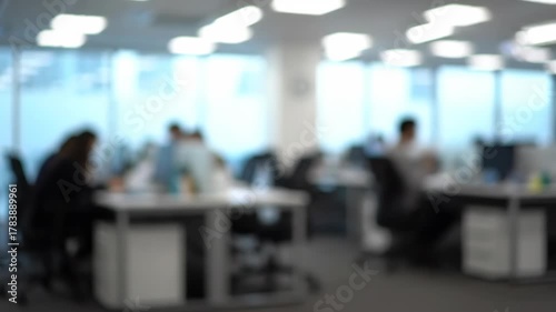 Blurred Office Space - The video shows a blurred office environment with employees working at their desks. The modern space is bright with natural light coming from the windows.