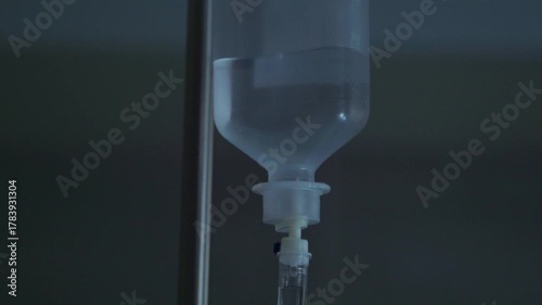 Close up of an intravenous drip bag hanging on a metal pole, with saline solution flowing into a tube for medical treatment in a hospital room, illustrating healthcare and recovery concepts