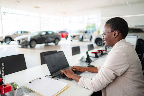 Wallpaper Mural Smiling saleswoman using laptop in car dealership Torontodigital.ca