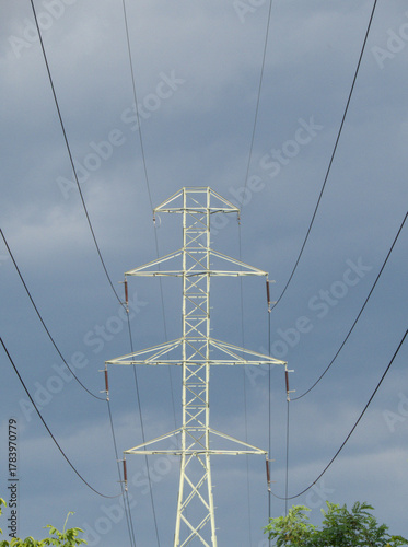 Tall electricity transmission tower with power lines against cloudy sky, industrial infrastructure view.