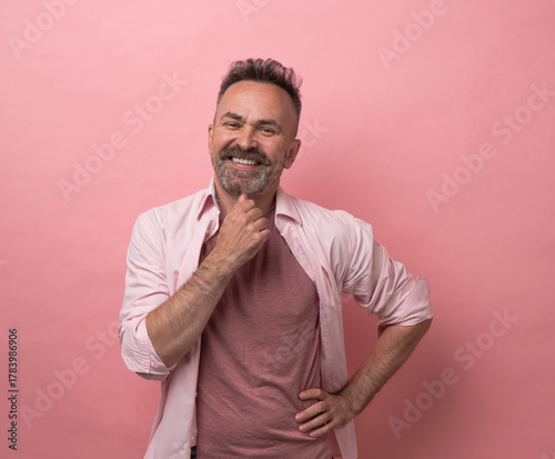 Middle age man with mustache posing with hand on chin smiling and happy expression. portrait of mature man 50yo with short cut-hair isolated pink pastel background