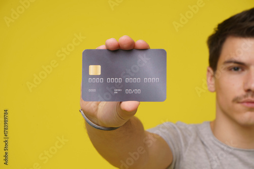 A young man, wearing a casual t-shirt, holds a credit card towards the camera, his mouth open in surprise