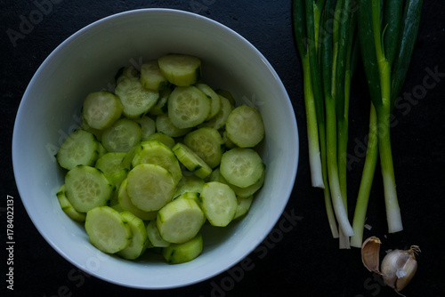 A white plate filled with sliced cucumber, green onions, and garlic