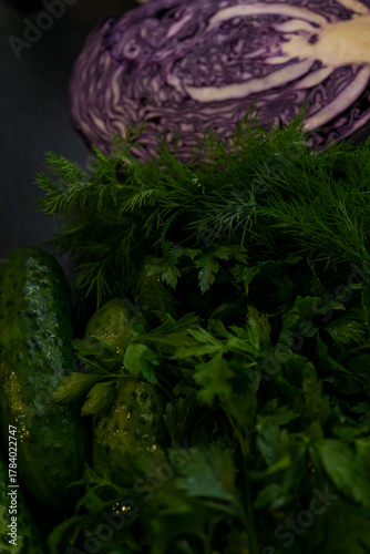 Several cucumbers and herbs in close-up. Red cabbage is in the background