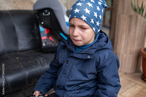 Upset young boy crying loudly with tears running down his face, wearing a star-patterned hat and a navy blue jacket outdoors