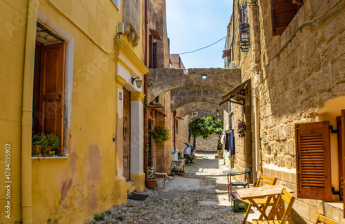 Fototapeta Naklejka Na Ścianę i Meble -  Narrow cobblestone alley with stone arches and yellow walls in the Rhodes Old town, Greece