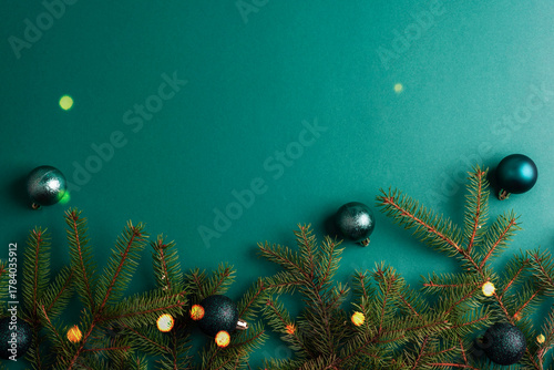 Christmas composition with fir branches, glitter and green baubles on a green background. Top view, flat lay, copy space