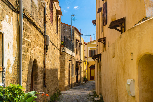 Fototapeta Naklejka Na Ścianę i Meble -  Narrow cobblestone alley  with yellow stone walls in the Rhodes Old town, Greece