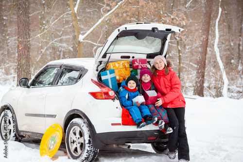 Smiling mom with her kids surrounded by holiday gift boxes in back of snowy car, enjoying magical winter forest day. Merry Christmas