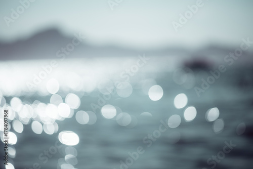 Shimmering sea surface captured out of focus with sparkling bokeh reflections and a distant horizon, evoking dreamy coastal light and abstract seaside texture