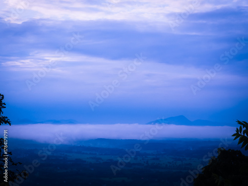 A breathtaking morning mist covering the mountain top during the rainy season. The soft fog drifts over lush green forests under a calm sky  
