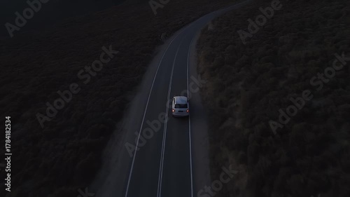 Aerial View of a Car Driving on a Winding Road Through Dark Hills During a Pink and Purple Sunset Sky