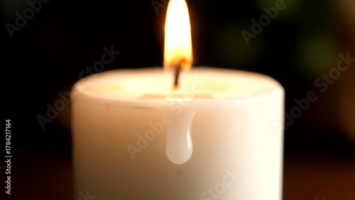 Close-up of a burning white candle with wax dripping, set against a blurred green background