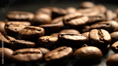 Close-up of roasted coffee beans scattered on a dark surface, highlighting their rich texture and color